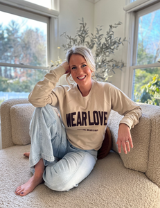 Jordan Strobeck wearing a Wear Love® sweatshirt sitting on a couch in a bright room with large windows.