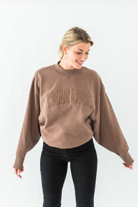 Woman wearing a brown sweatshirt with 'WEAR LOVE' text on a white background