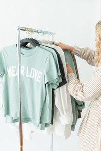 Woman selecting t-shirts from a rack with 'Wear Love®' text on a light background